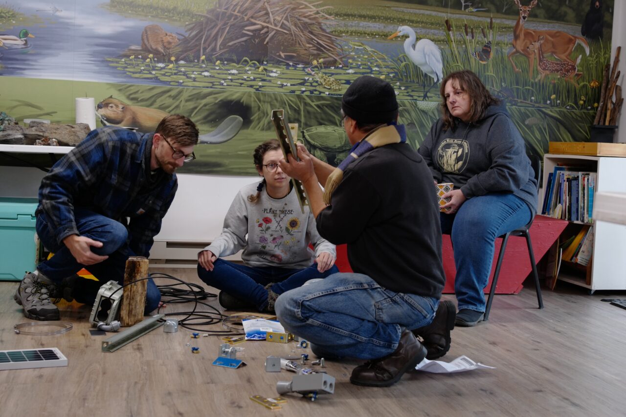 Four people sitting around in a floor building infrastructure for a FieldKit installation. Many tools and pieces of hardware are strewn about.